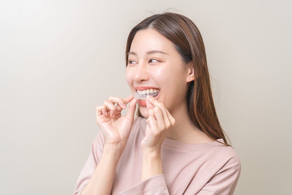 A woman smiles while holding a clear aligner near her teeth, preparing to place it in her mouth - Washington Orthodontics