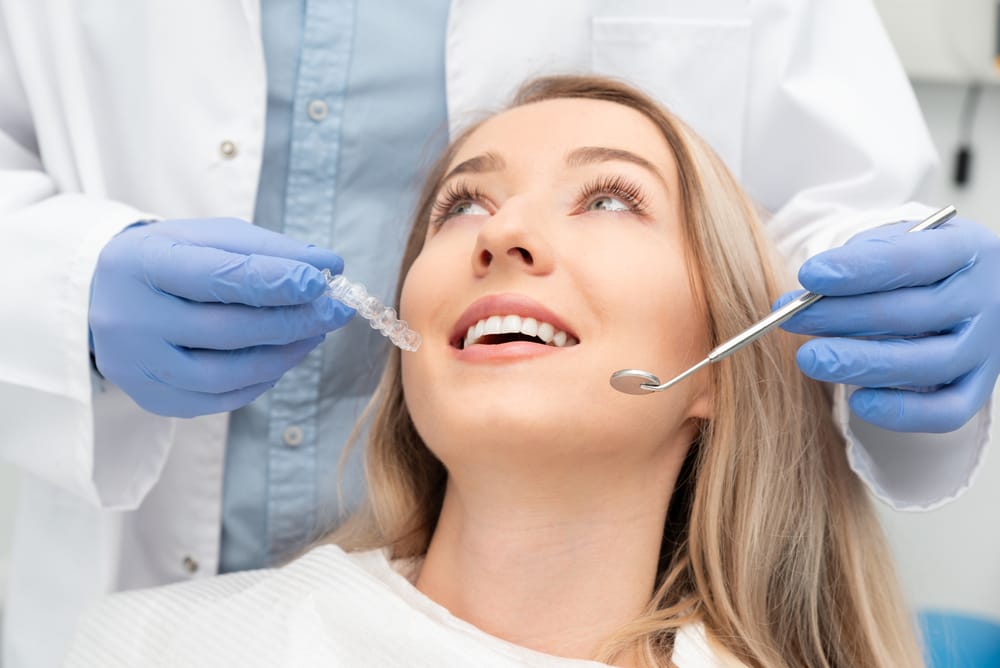 An orthodontic patient smiling during a consultation as the doctor holds a clear aligner, highlighting personalized orthodontic care and advanced treatment options – Washington Orthodontics.